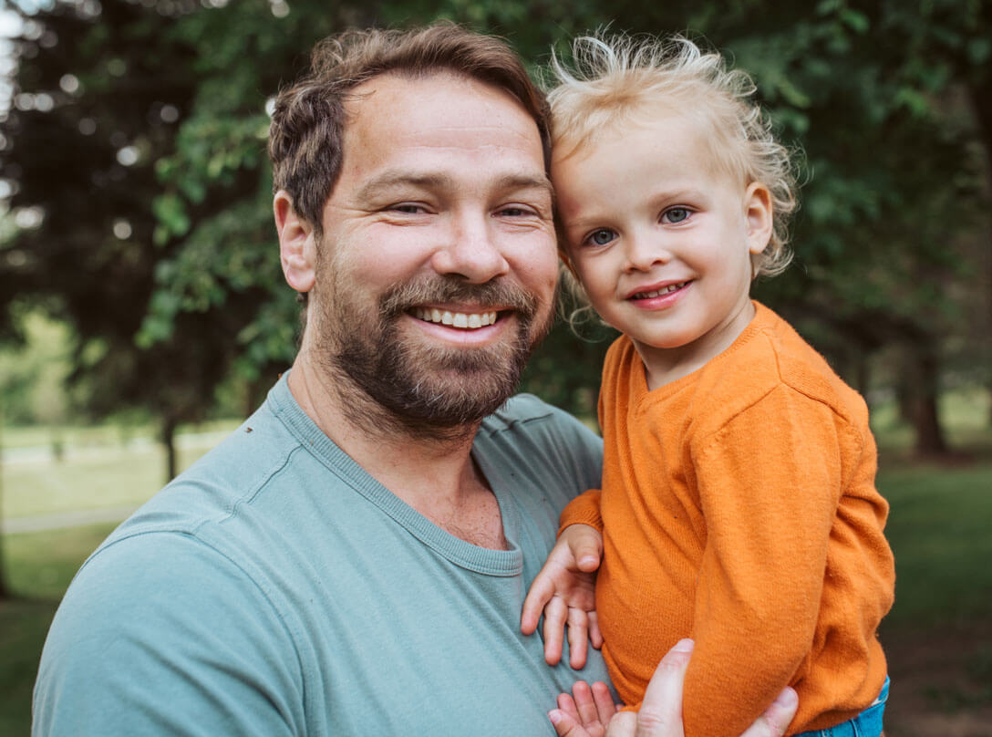 Ein Vater mit Kind auf dem Arm zeigt, wie Wirtschaftsprüfer für finanziellen Wohlstand für ihn und seine Familie sorgen.